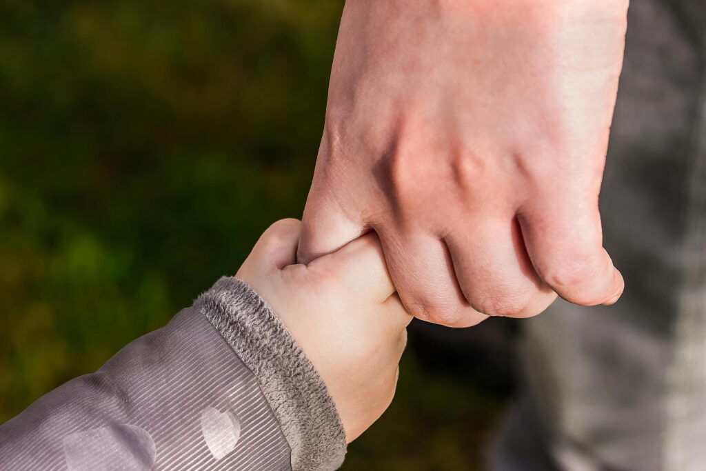A close-up of a child and parent holding hands in a park, symbolizing love and trust.